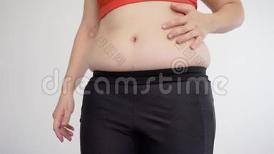 穿着运动服的超重女人捏着她的腹部脂肪。 纤维素和暴饮暴食